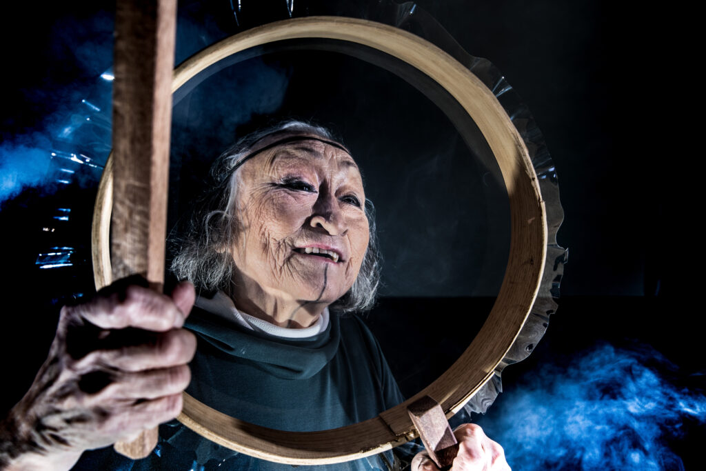 En kvindes ansigt er indrammet af en hul grønlandsk tromme.